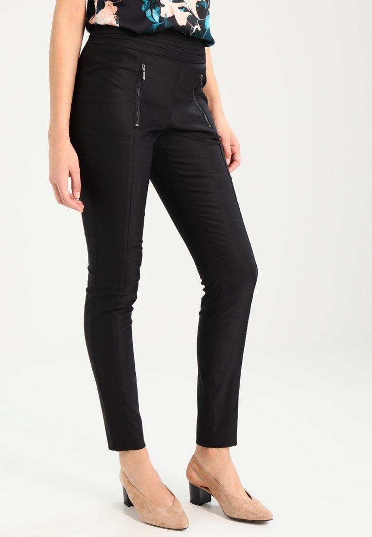 Svarta slim-fit byxor i en mjuk tygkvalitet, med fickor med dragkedja framtill och hög midja. Matchade med beige klackskor i blockmodell.