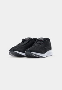 Chaussures de sport noires avec une tige en mesh pour la respirabilité, semelle intermédiaire blanche, semelle extérieure texturée noire et logo Tommy Hilfiger sur la languette.