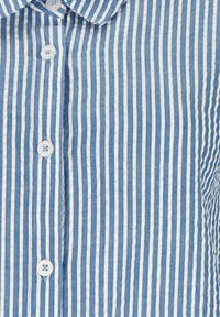 Camicia a righe verticali blu e bianche con bottoni frontali, colletto arrotondato e tessuto testurizzato. I bottoni sono bianchi con un design a quattro fori.
