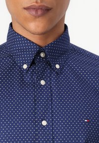 Marineblauw overhemd met knopen, versierd met een klein wit en blauw geometrisch patroon, puntige kraag en een merklogo detail op de borst.