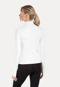 Long-sleeve, white fitted top with a high collar and thumbholes. Smooth texture and sleek design tailored for active wear.