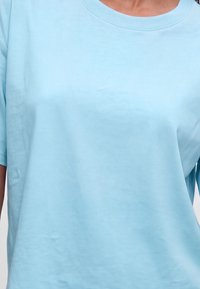 Άτομο με απλό ανοικτό μπλε βαμβακερό T-shirt με στρογγυλή λαιμόκοψη και κοντά μανίκια.