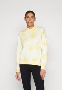 Sweat à capuche tie-dye jaune clair, en tissu doux, à manches longues, avec capuche à cordon de serrage réglable, poignets et ourlet côtelés, assorti à des leggings noirs.