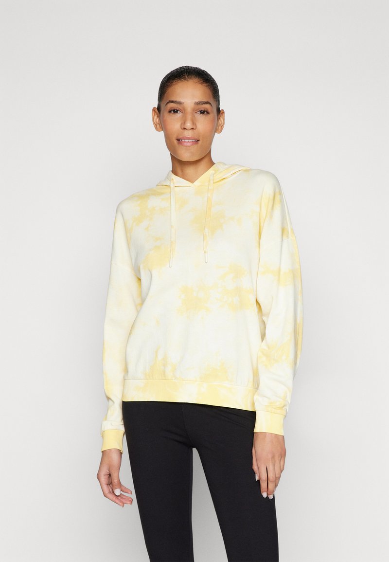 Sweat à capuche tie-dye jaune clair, en tissu doux, à manches longues, avec capuche à cordon de serrage réglable, poignets et ourlet côtelés, assorti à des leggings noirs.