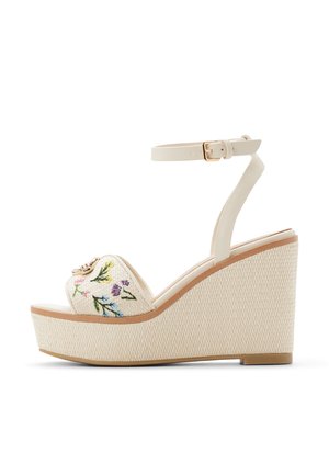 Witte platformsandalen met geborduurde bloemenpatronen aan de voorkant, voorzien van een bijpassende enkelriem en een textuurrijke sleehak.