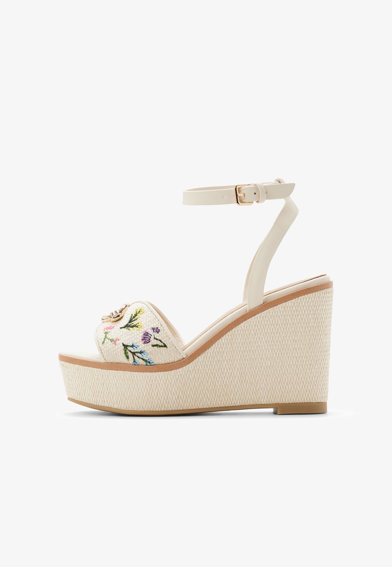 Witte platformsandalen met geborduurde bloemenpatronen aan de voorkant, voorzien van een bijpassende enkelriem en een textuurrijke sleehak.