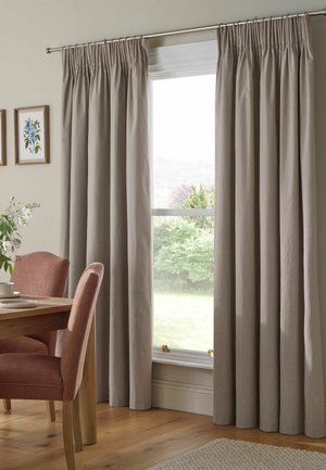 Beige, bodenlange Vorhänge hängen an einer Metallstange über einem Fenster in einem Esszimmer mit einem Holztisch und rosa gepolsterten Stühlen.