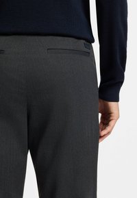 Gray tailored trousers featuring a textured fabric, straight cut, and two back pockets. Worn with a navy sweater.