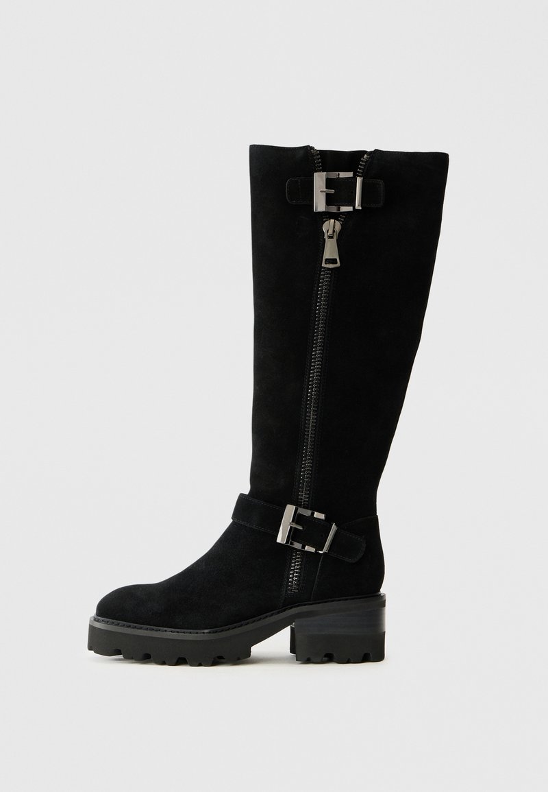 Botas de ante negras hasta la rodilla. Cuenta con un cierre de cremallera lateral, un detalle de hebilla en el puño y una suela gruesa y estriada para mayor tracción.