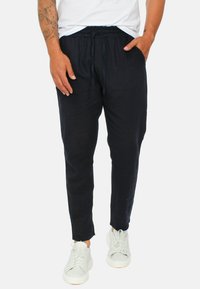 Pantaloni navy con coulisse realizzati in tessuto leggero, design a gamba affusolata, con tasche laterali e vestibilità casual. Indossati con sneakers bianche.