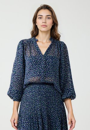 Navy blauw, doorzichtige blouse met een V-hals, puffed sleeves en verspreide groene en witte stippen. Zachte textuur, lichtgewicht stof.