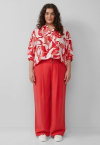 Rood-wit gestreepte shirt met een losse pasvorm, gecombineerd met felrode wijde broek en witte schoenen, wat zorgt voor een samenhangende uitstraling.