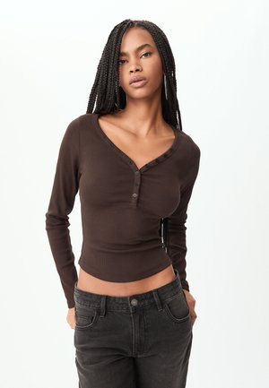 Maglione marrone a maniche lunghe con una texture a coste, scollatura a V e cinque bottoni lungo la parte anteriore. Abbinato a jeans neri a vita alta.
