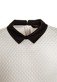 Helles, strukturiertes Stoffoberteil mit einem schwarzen Satin-Kragen, versehen mit einem Reißverschluss auf der Rückseite und einem geometrischen Muster auf dem Körper.