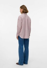 Geverfd shirt in roze en wit, met lange mouwen, knoopmanchetten en een relaxte pasvorm, gecombineerd met blauwe flare jeans en bruine schoenen.