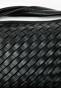 Borsa a mano nera in pelle intrecciata con superficie testurizzata e manico curvo ed elegante. Il motivo è costituito da strisce intrecciate complesse.