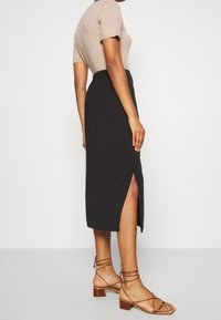 Černá midi sukně s bočními rozparky, elastickým páskem, nošená s přiléhavým béžovým topem a hnědými sandály na podpatku. Hladký textilní vzhled.