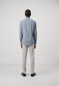 Hellblaues Langarmhemd mit einem dezenten Muster, taillierte Passform und Knopfmanschetten, kombiniert mit hellen Hosen und schwarzen Schuhen.