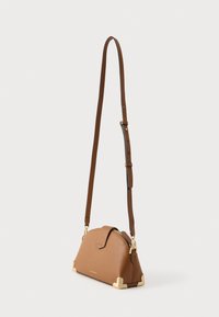 Barna bőr keresztpántos táska ívelt formával, arany színű fém kiegészítőkkel, patentos zárral és állítható pánttal. Sima textúra.