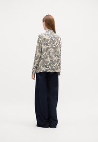 Long-sleeve shirt with a paisley pattern in beige and blue. Soft fabric, relaxed fit, curved hem. Paired with wide-leg dark denim pants.