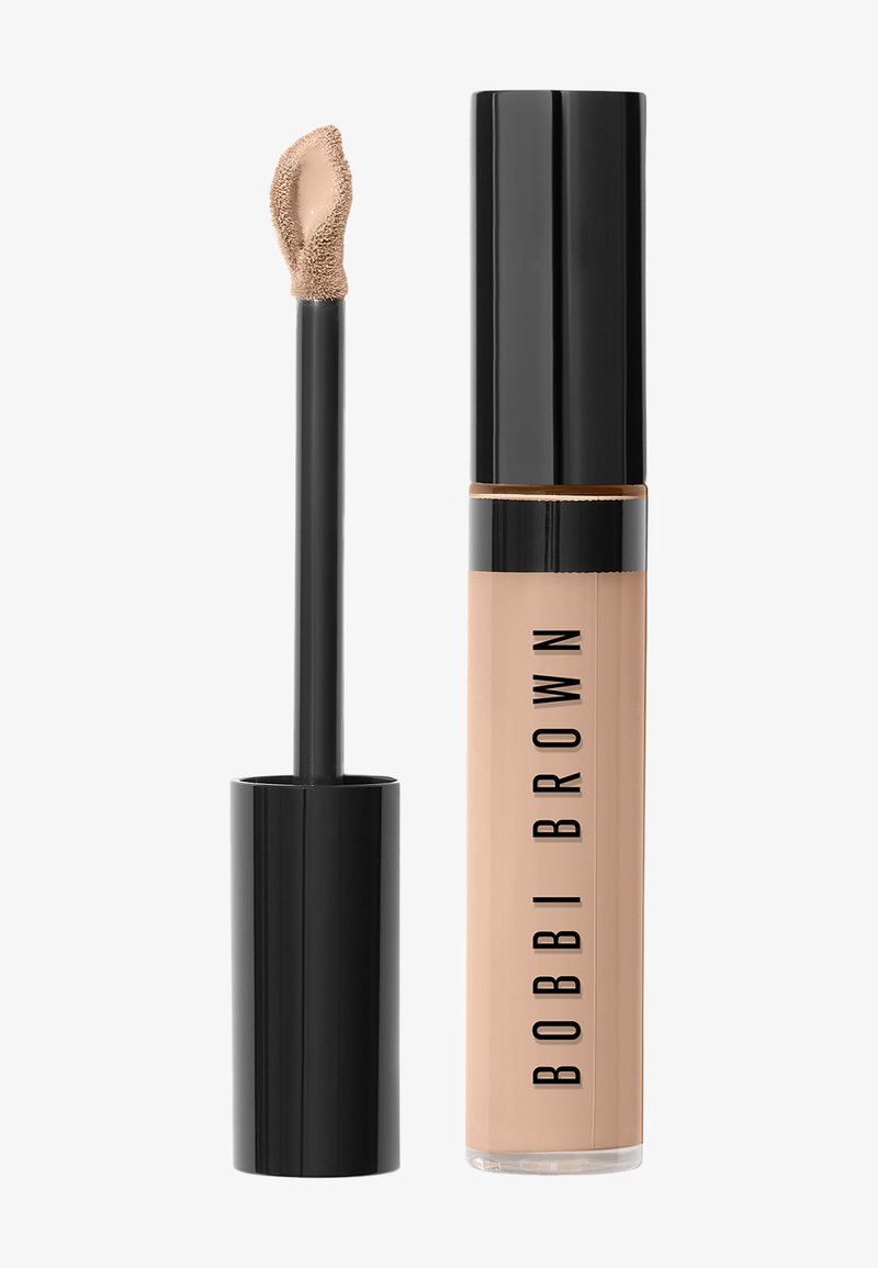 Flüssiger Concealer mit schwarzem Deckel und Applikator mit Flockspitze, beiger Farbton, auf der durchsichtigen zylindrischen Tube mit der Aufschrift "Bobbi Brown".