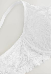 Bralette bianco in pizzo con motivi floreali, orlo a scallop e spalline regolabili. Texture morbida e design leggero.