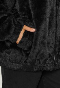 Czarna kurtka z sztucznego futra o miękkiej fakturze, z suwakiem i bocznymi kieszeniami. Rękawy są ściągane, a dół jest lekko elastyczny.