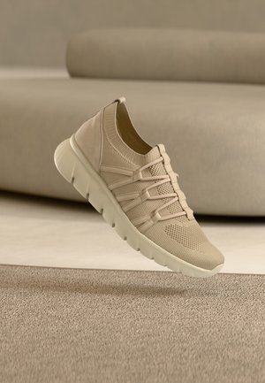 Beiger Sportschuh mit Mesh-Obermaterial, elastischem Schnürsystem und strukturiertem Profil. Abgerundete Zehenform und gepolsterter Fersenbereich. Leichtes Material.