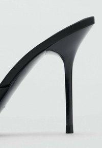 Sandalia negra de tacón alto con un diseño elegante, punta puntiaguda y tacón de aguja delgado. Textura suave y silueta minimalista.