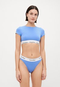 Šviesiai mėlyna trumpa palaidinė su trumpomis rankovėmis derinama su šviesiai mėlynomis kelnaitėmis, turinčiomis baltą Calvin Klein logotipo juostelę. Minkšta, elastinga medžiaga.