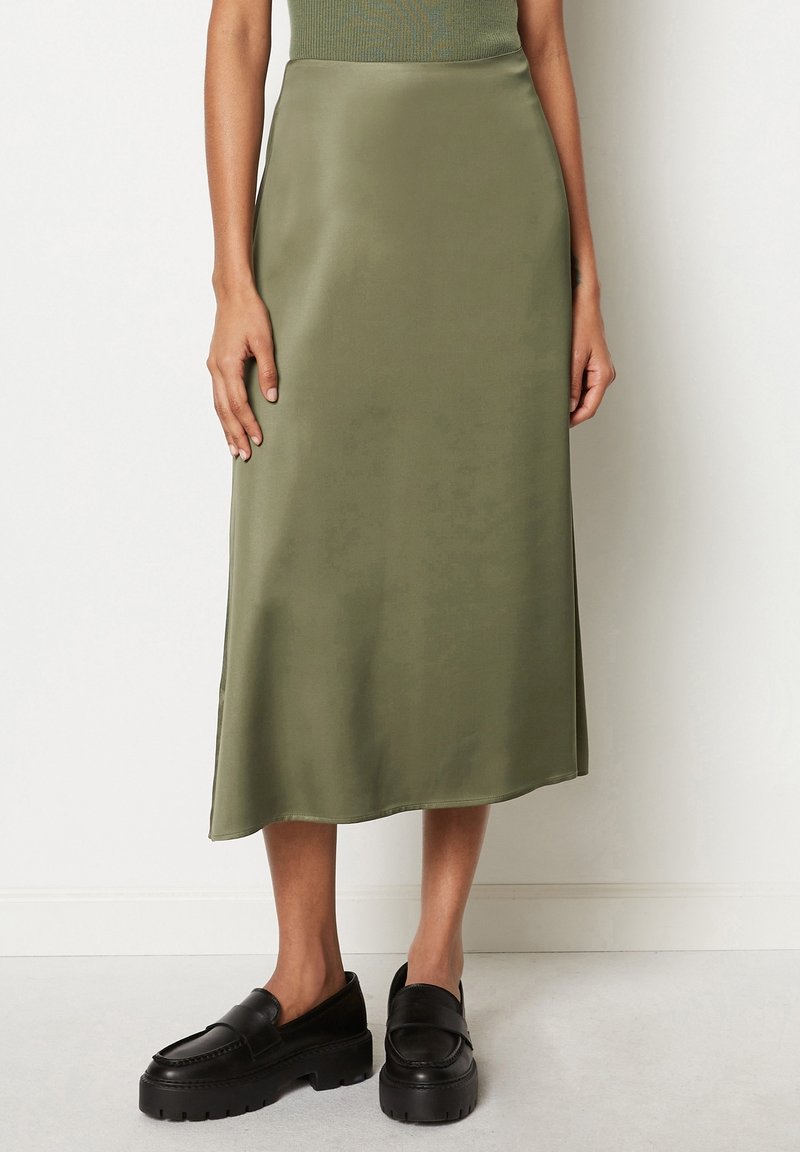 Falda midi de satén verde oliva con una textura suave y un corte recto, combinada con mocasines negros de suela gruesa. Diseño simple y elegante.