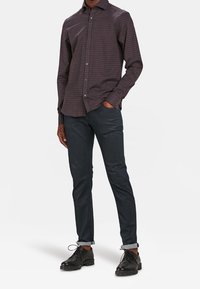 Košile s dlouhým rukávem v tmavých kostkovaných vzorech se standardním límcem, spárovaná s úzkými tmavými denimovými džíny a černými šněrovacími botami, s vyhrnutými manžetami.