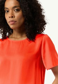 Czerwona jedwabna bluzka z krótkimi rękawami i okrągłym dekoltem, charakteryzująca się gładką, błyszczącą teksturą i minimalną ilością szwów.