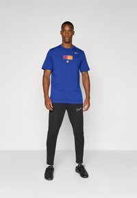 Blå bomulds t-shirt med et vandret stribet Barcelona-logo, parret med sorte træningsbukser med en hvid Nike swoosh.