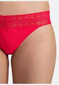 Tanga rosso di cotone con cinturino in pizzo caratterizzato da un motivo geometrico. Texture liscia e design aderente progettato per il massimo comfort.