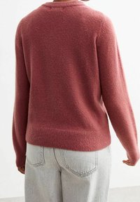 Tät, crew-neck tröja i mjukt, texturerat rosafärgat tyg, med ribbade ärmmuddar och fåll, i kombination med ljusgrå högmidjade jeans.