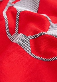 Close-up van rood textiel met een verhoogd wit en zwart gestippeld ontwerp dat een gestileerd abstract patroon vormt.