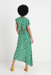 Grön blommig maxiklänning med volangärmar, öppen rygg och figurnära midja. Tyget har ett litet blommönster.