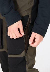 Technische outdoorbroeken met een mix van olijfgroen en zwarte stof, ritszakken met mesh voering en versterkte stikdetails.