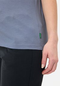 Gray, short-sleeve t-shirt with a smooth texture and side green label, paired with black pants; focus on fabric and color details.