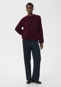 Pull en tricot bourgogne avec des manches larges, associé à un jean droit navy. Le look est complété par des chaussures noires. Design et texture simples.