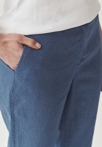 Pantalones azules con un estampado, fabricados en un tejido ligero, que presentan un diseño texturizado con pequeños puntos blancos y un detalle de bolsillo lateral.