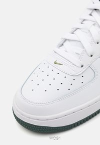 Białe skórzane sneakersy z perforowanym noskiem, zieloną gumową podeszwą i subtelnym haftowanym zielonym logo z boku. Wiązanie z grubymi sznurowadłami.