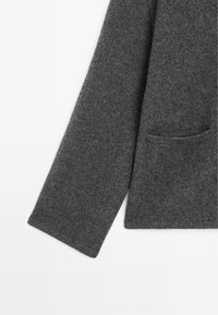 Giacca in misto lana grigio scuro con una sola tasca, maniche lunghe e una finitura morbida e testurizzata. Design semplice e pulito, privo di abbellimenti.