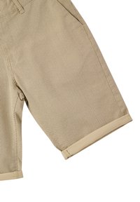 Shorts beige in rete con un tessuto testurizzato, dotati di orli arrotolati e tasche laterali. Il design enfatizza la traspirabilità e il comfort.