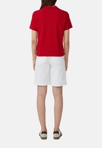 Rode korte mouwen polo, witte shorts tot de knie en casual sneakers. Het shirt heeft een kraag en een zachte textuur.