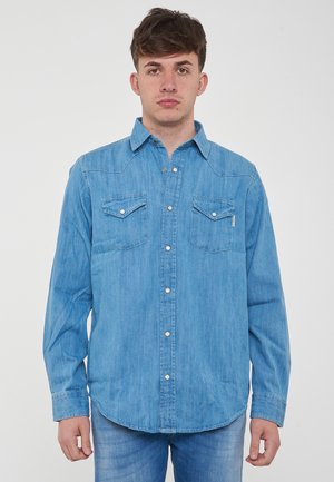 Camicia di denim azzurro chiaro con colletto button-down, due tasche sul petto e bottoni bianchi. Presenta maniche lunghe e un orlo curvo.
