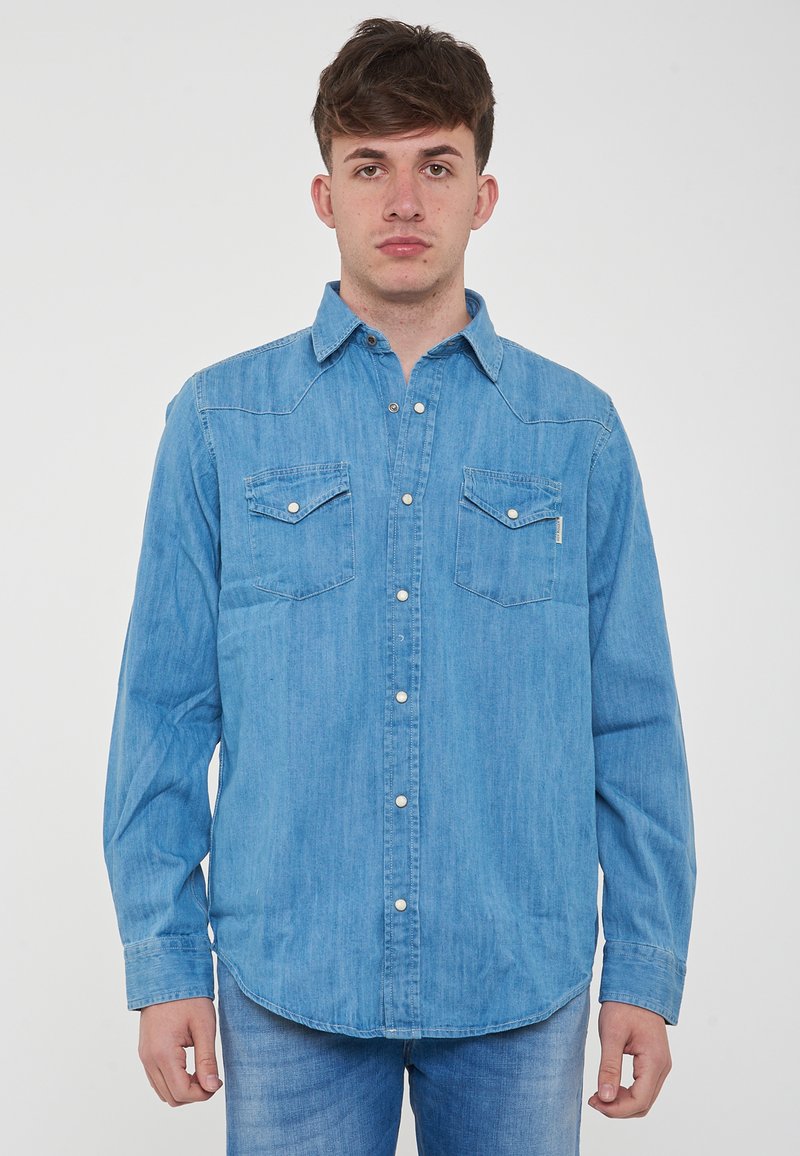 Camicia di denim azzurro chiaro con colletto button-down, due tasche sul petto e bottoni bianchi. Presenta maniche lunghe e un orlo curvo.