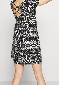 Robe à motifs noir et blanc avec des dessins géométriques, une silhouette ajustée et un dos ouvert avec des bretelles croisées.