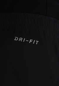 Pantalones cortos DRI-FIT negros con una textura suave, cinturilla elástica y letras reflectantes en el lateral. Adecuados para un uso activo.